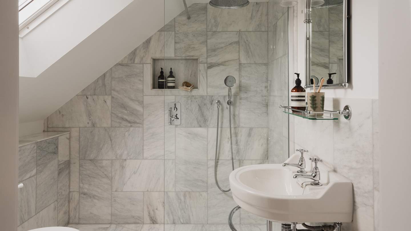 The en suite shower room with a walk-in rainfall shower is adorned with luxe marble tiles