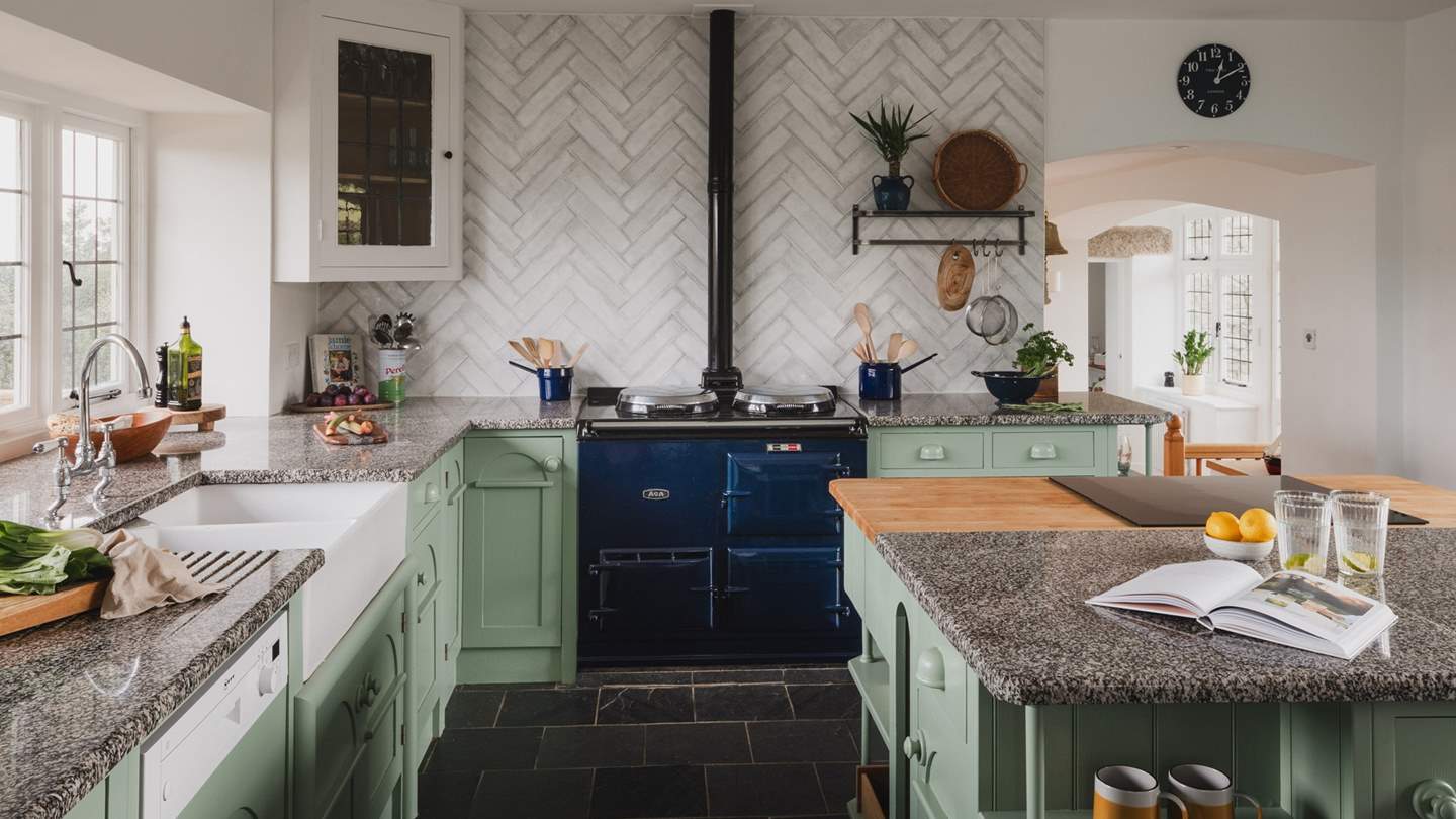 Herringbone tiles adorn a feature wall and soft green cabinetry with polished stone worktops offer ample space for crafting repasts