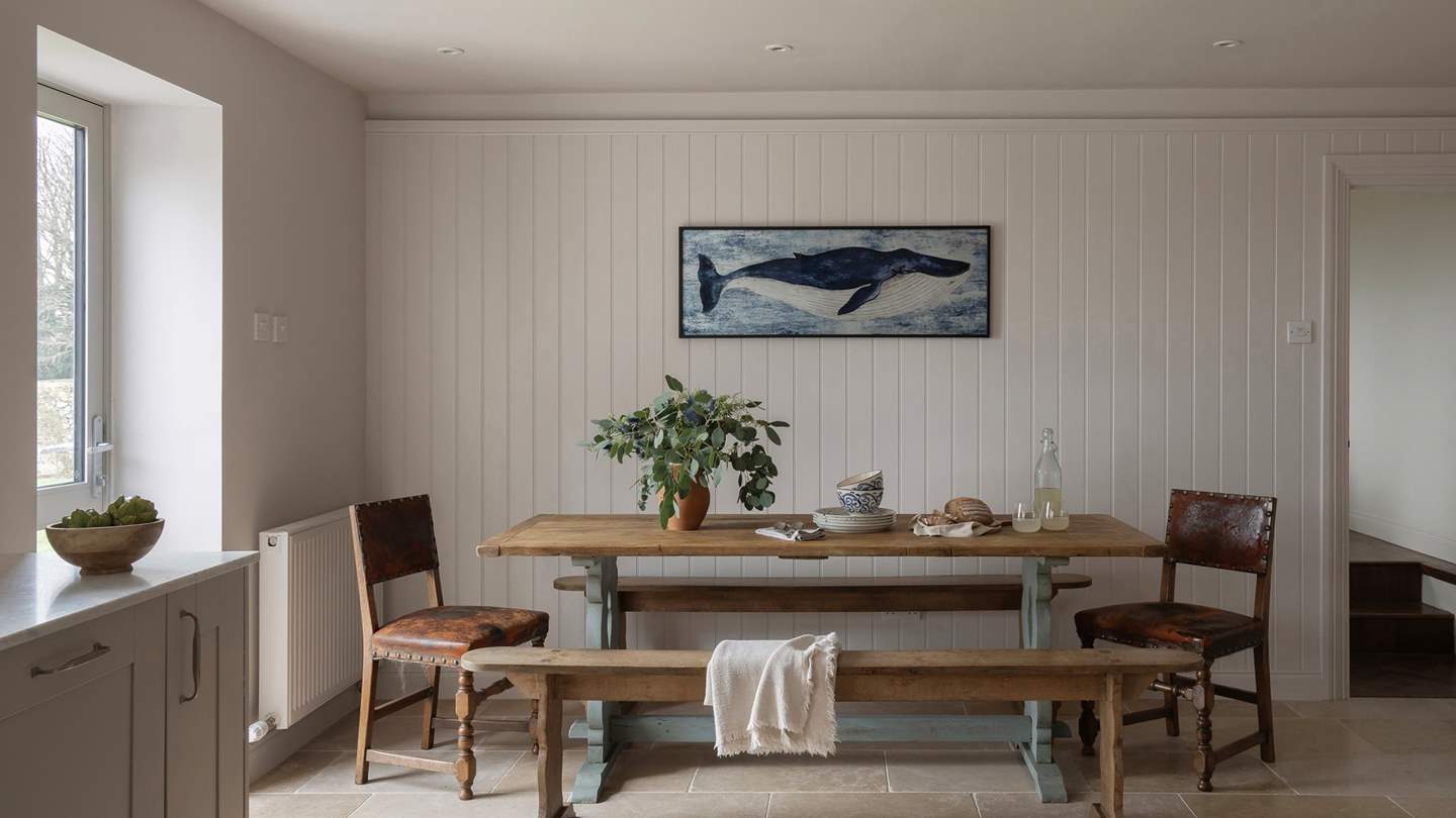 Beckoning for appetisers and aperitifs, a farmhouse dining table with bench seating and two chairs resides in the kitchen