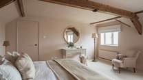The stunning fourth bedroom is pretty as a picture with rose tones and exposed wood