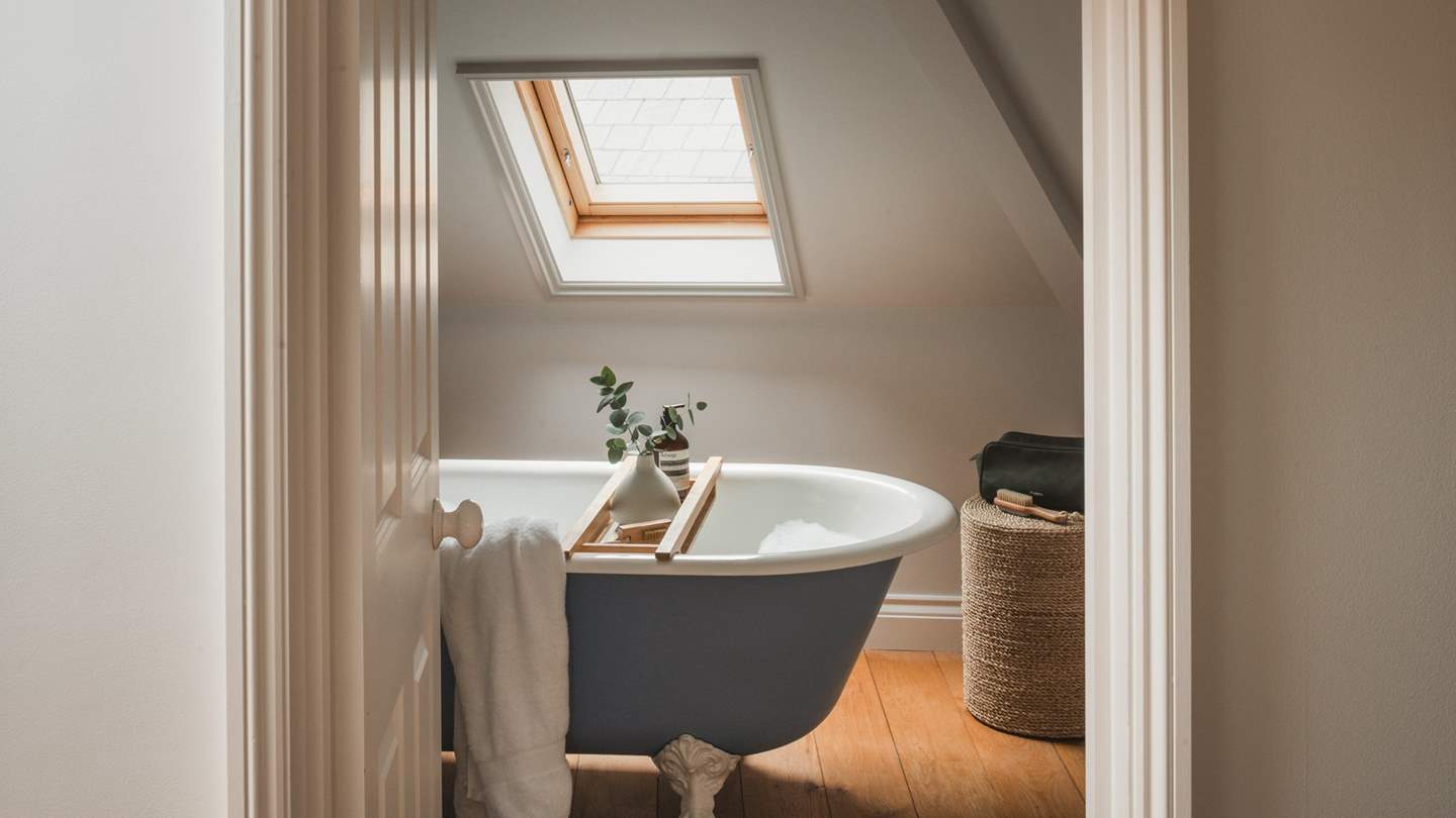 This bathroom benefits from a freestanding rolltop bath in shades of white and blue, idyllic for soothing soaks under the skylight