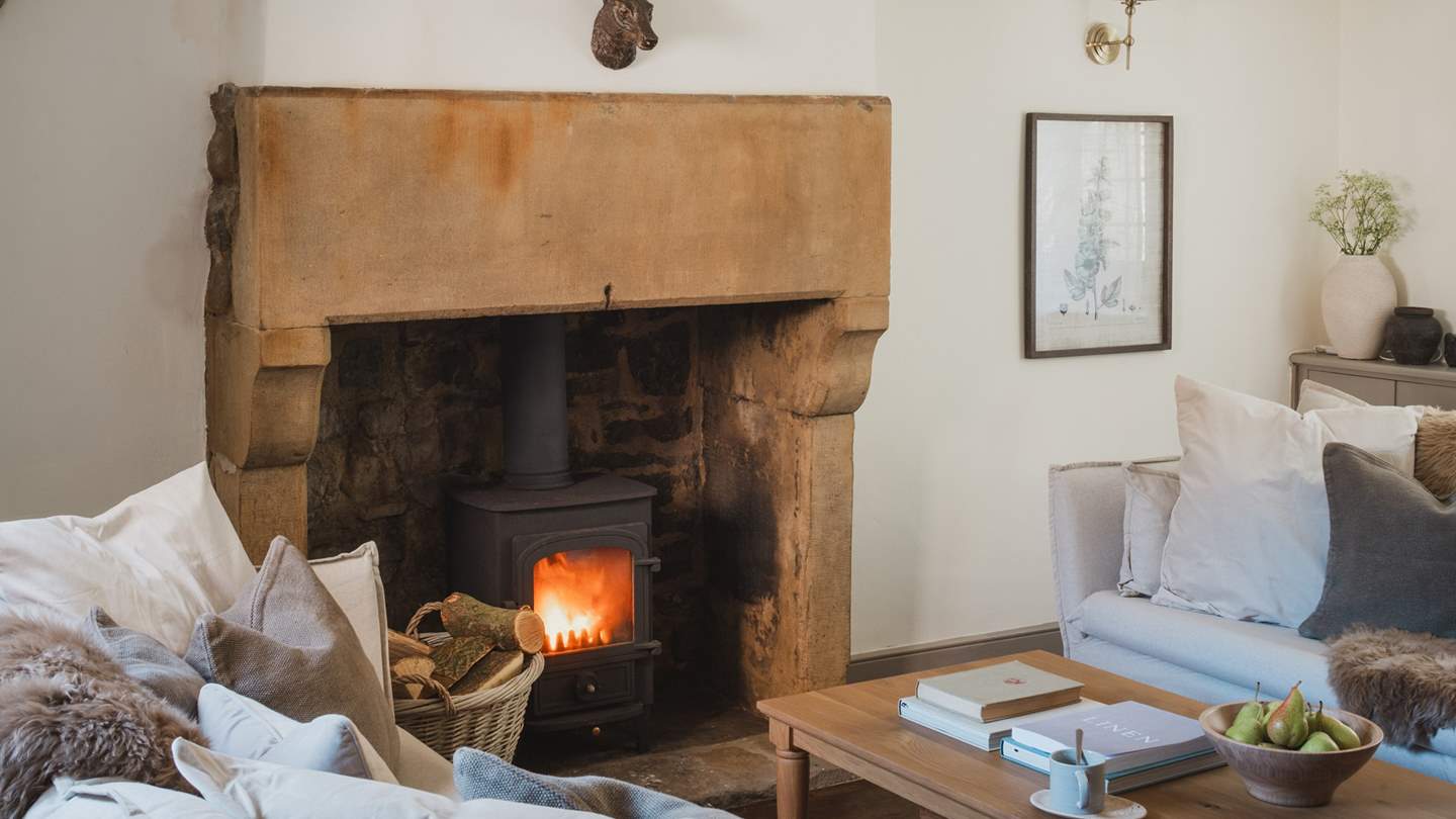 A wood burning stove is set within a rustic inglenook fireplace