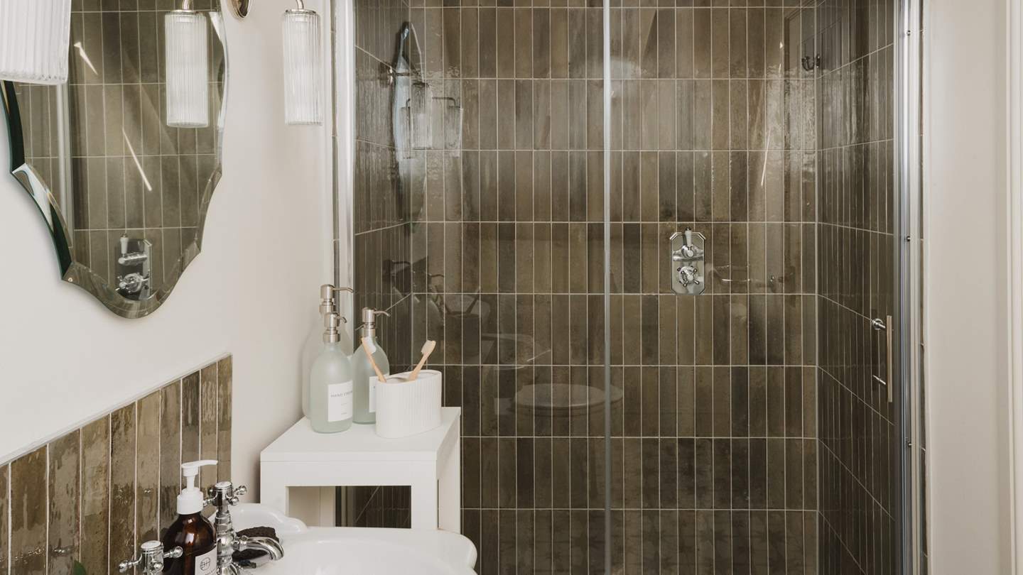 A walk-in rainfall shower with glossy olive-toned tiles awaits