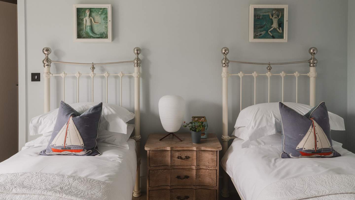Featuring two 3ft white wrought iron single beds by Cornish Bed Co, this bedroom overlooks the leafy surrounds, with coastal glimpses in the distance... 