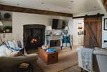 Two sofas and a deep armchair rest before a wood burning stove, ready for fireside moments bathed in an amber glow
