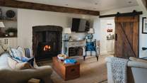 Two sofas and a deep armchair rest before a wood burning stove, ready for fireside moments bathed in an amber glow