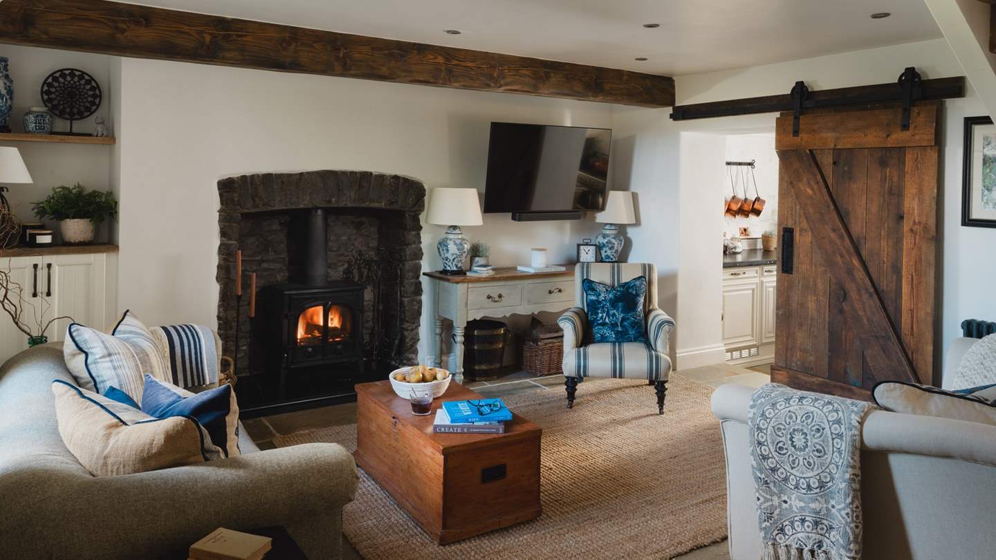 Two sofas and a deep armchair rest before a wood burning stove, ready for fireside moments bathed in an amber glow