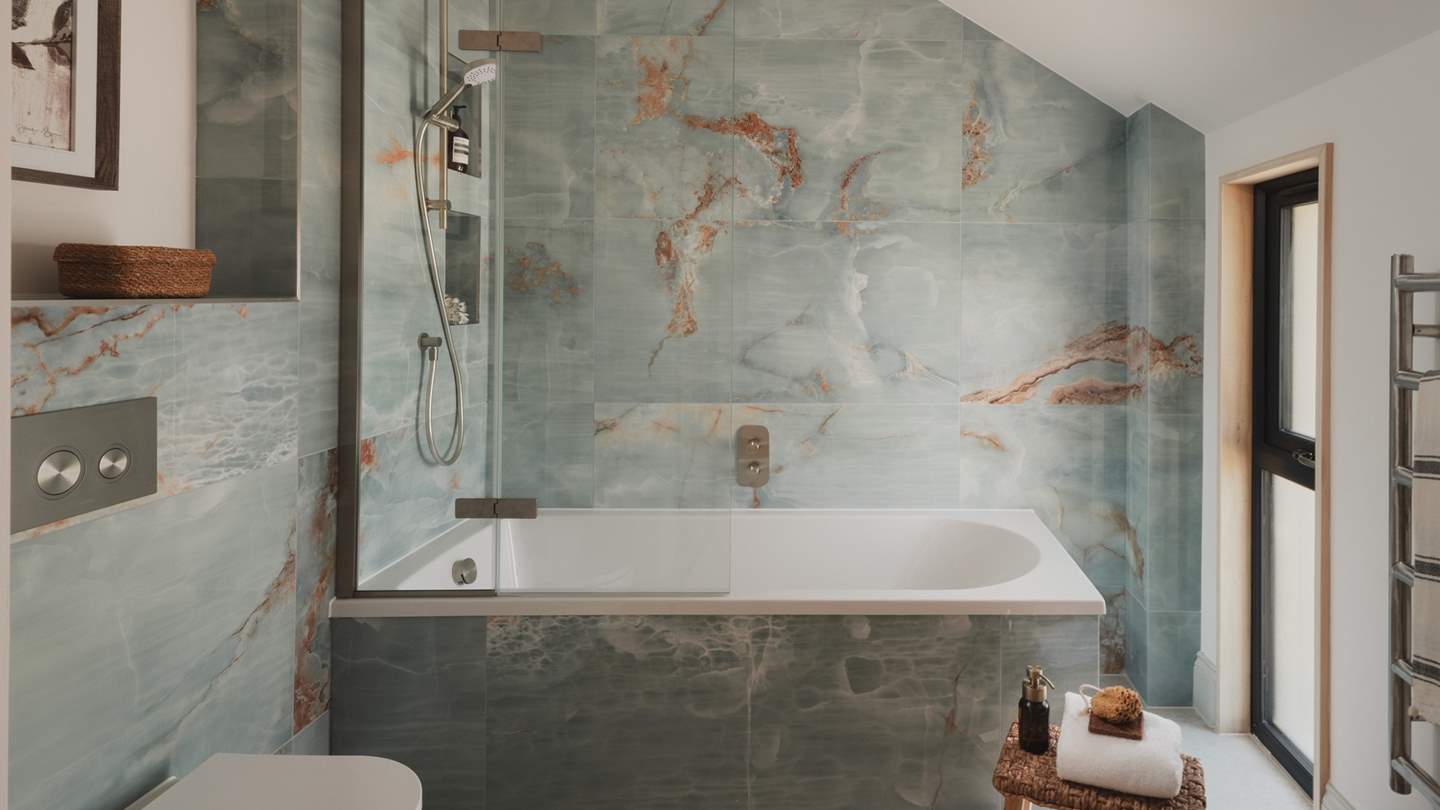 Positioned on the first floor, the family bathroom is beautifully designed with tiles in a calming palette inspired by the coast