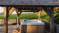 Beneath the wooden pergola resides an Urban Cedar hybrid hot tub 