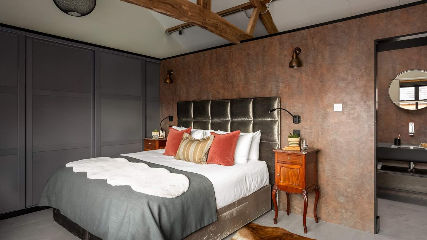 Nestled beneath striking vaulted ceilings and exposed beams, a king size bed beckons for restful slumber