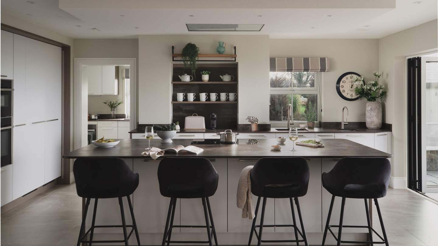 Opposite is the sleek kitchen, featuring glossy white cabinetry with chrome accents