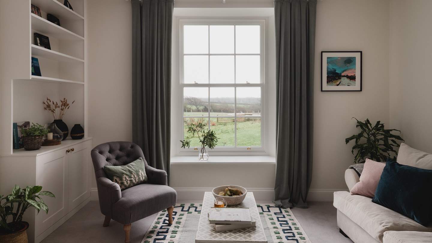 Wwo plush sofas in soft neutral tones and an armchair position perfectly beside a large sash window
