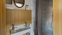 Adjacent is the en suite shower room, featuring mustard wood panelling and a walk-in rainfall shower, embellished with Calacatta marble metro tiles