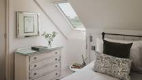 The bed is dressed with cushions and throws in verdant shades that complement the tranquil scenes beyond the Velux windows