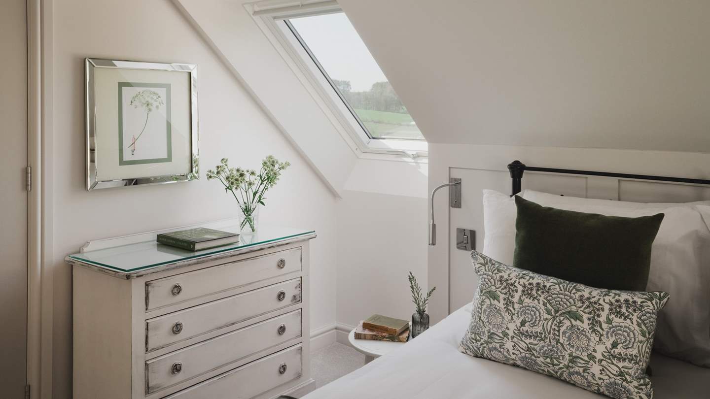 The bed is dressed with cushions and throws in verdant shades that complement the tranquil scenes beyond the Velux windows