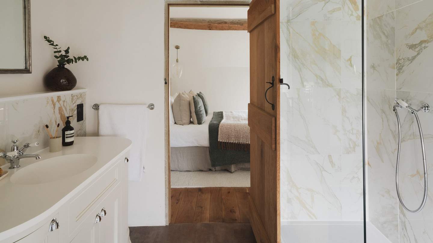 An ensuite bathroom proposes serene self-care rituals with marble hues and a walk-in shower