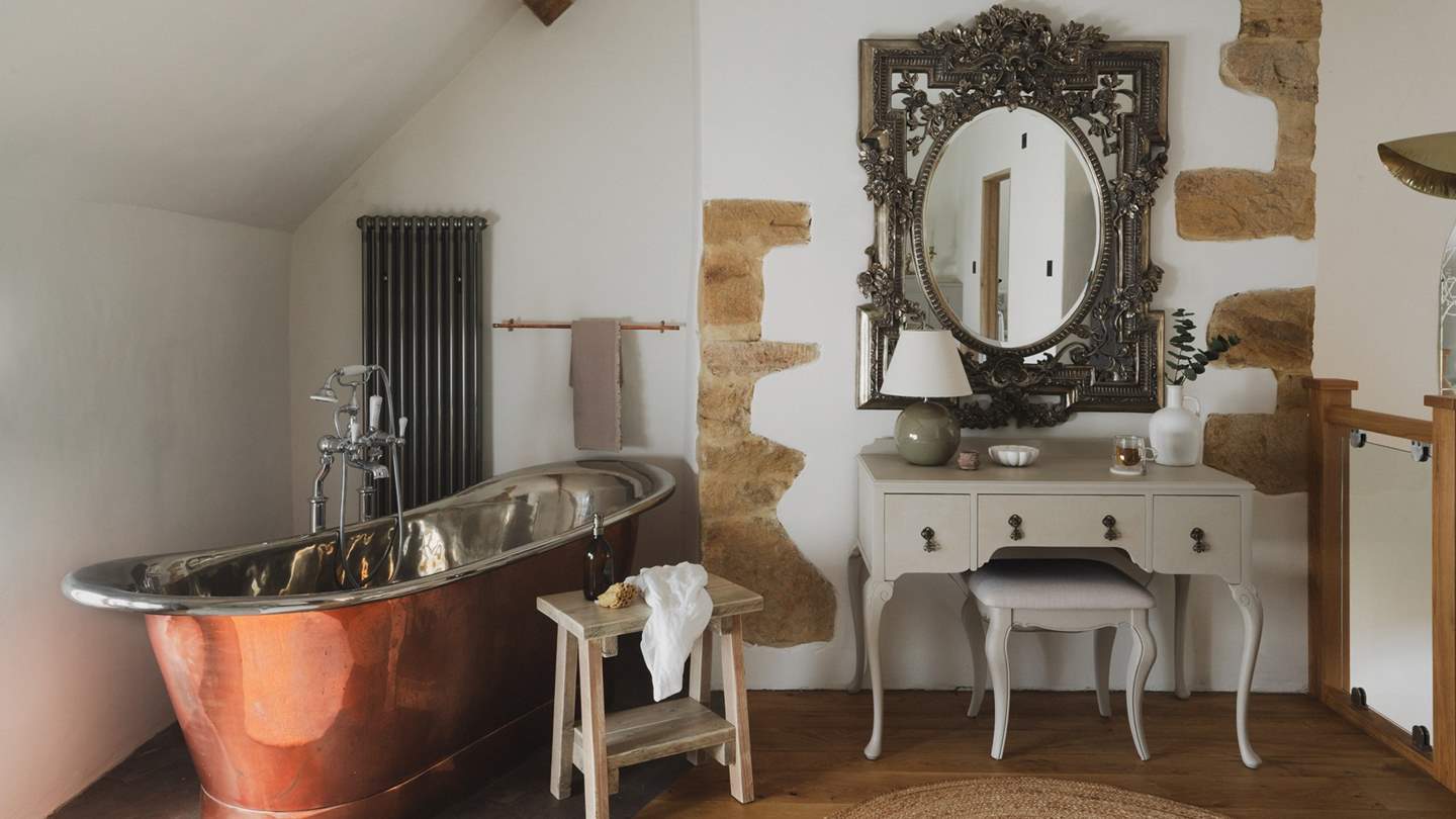 A vintage dressing table sits below an ornate, French giltwood-style mirror