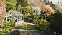 Beyond the courtyard, a tiered garden with a Victorian greenhouse stretches across the hillside