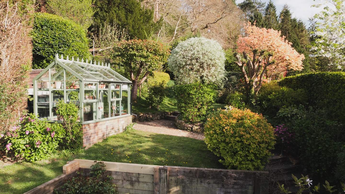 Beyond the courtyard, a tiered garden with a Victorian greenhouse stretches across the hillside
