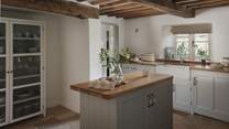 Bespoke cabinetry, wooden worktops and a central island rest beneath characterful exposed beams