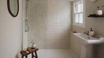 A spacious walk-in shower is adorned with creamy Zeligge tiles