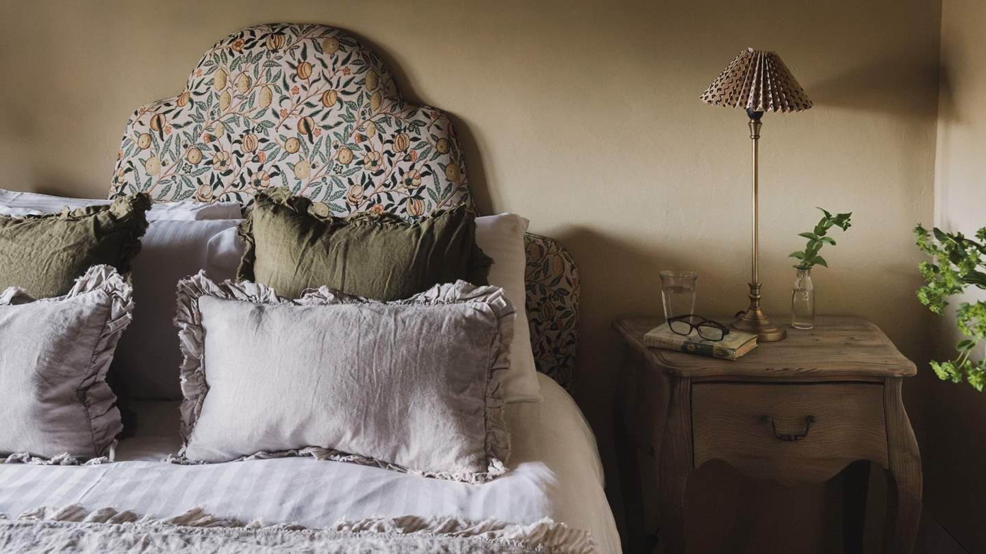 A double bed is framed by a William Morris headboard in complementary shades