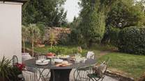 For alfresco dining, a large round table sits on the gravel pathway, accompanied by a Weber charcoal barbecue
