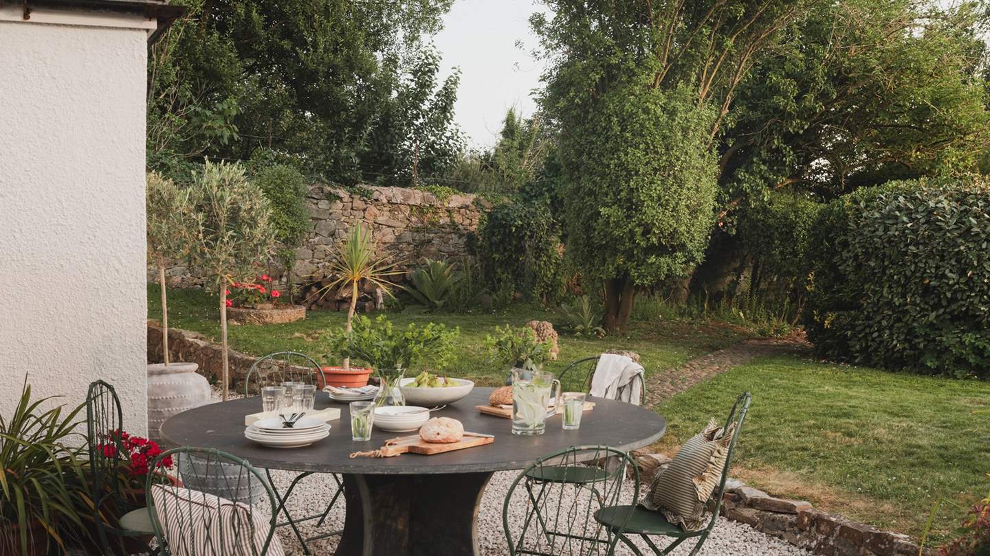 For alfresco dining, a large round table sits on the gravel pathway, accompanied by a Weber charcoal barbecue