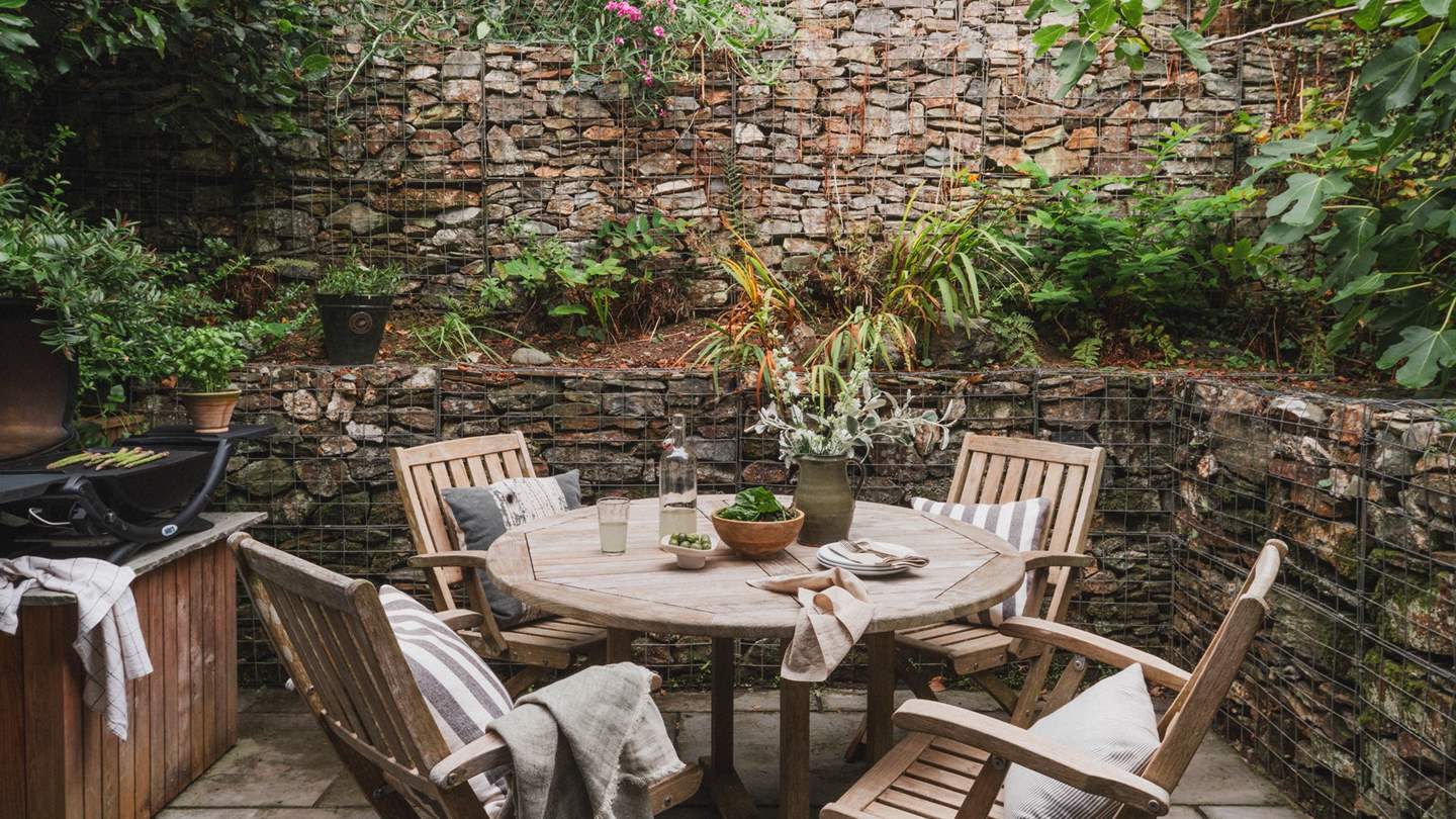 The pretty paved courtyard offers outdoor dining with a wooden table and chairs and Weber gas barbecue 