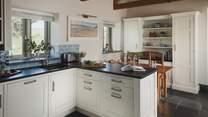 A timeless bespoke shaker-style kitchen, beautifully decorated in a charming hue of creamy white, boasts cool slate work surfaces and pale blue tiles

