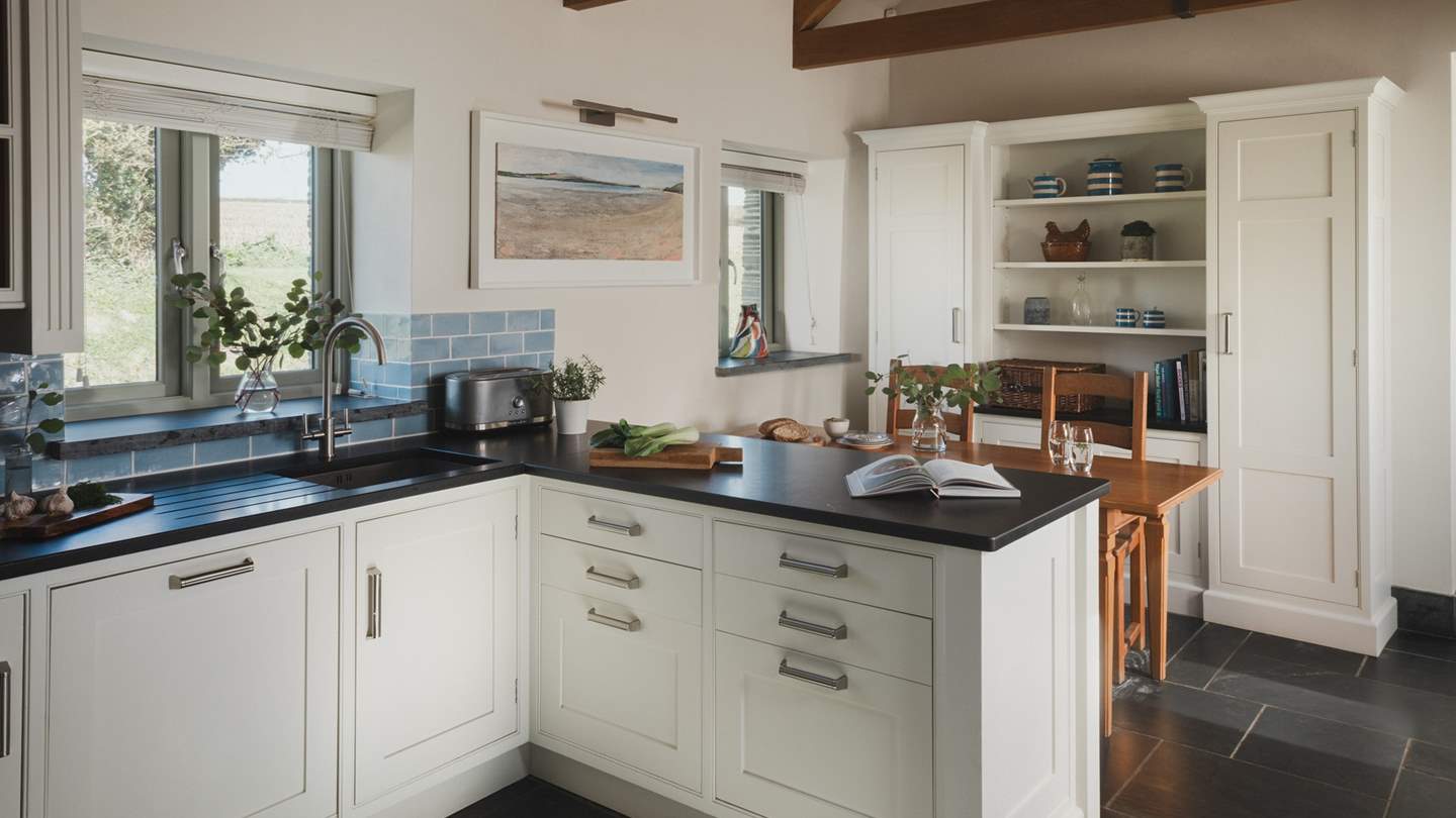 A timeless bespoke shaker-style kitchen, beautifully decorated in a charming hue of creamy white, boasts cool slate work surfaces and pale blue tiles

